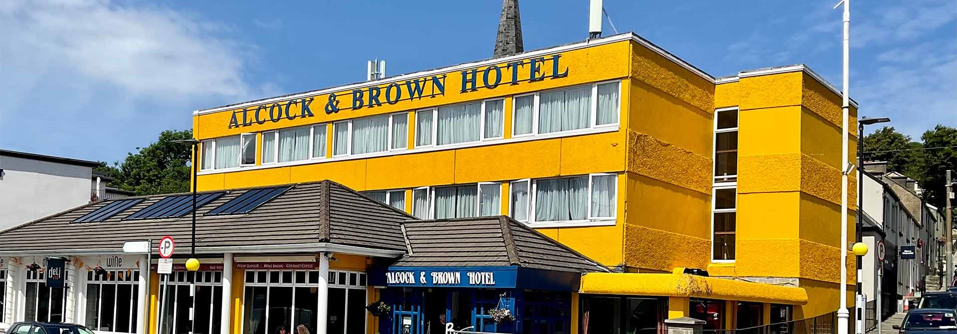 Bright yellow building labeled 'ALCOCK & BROWN HOTEL' with a blue entrance.