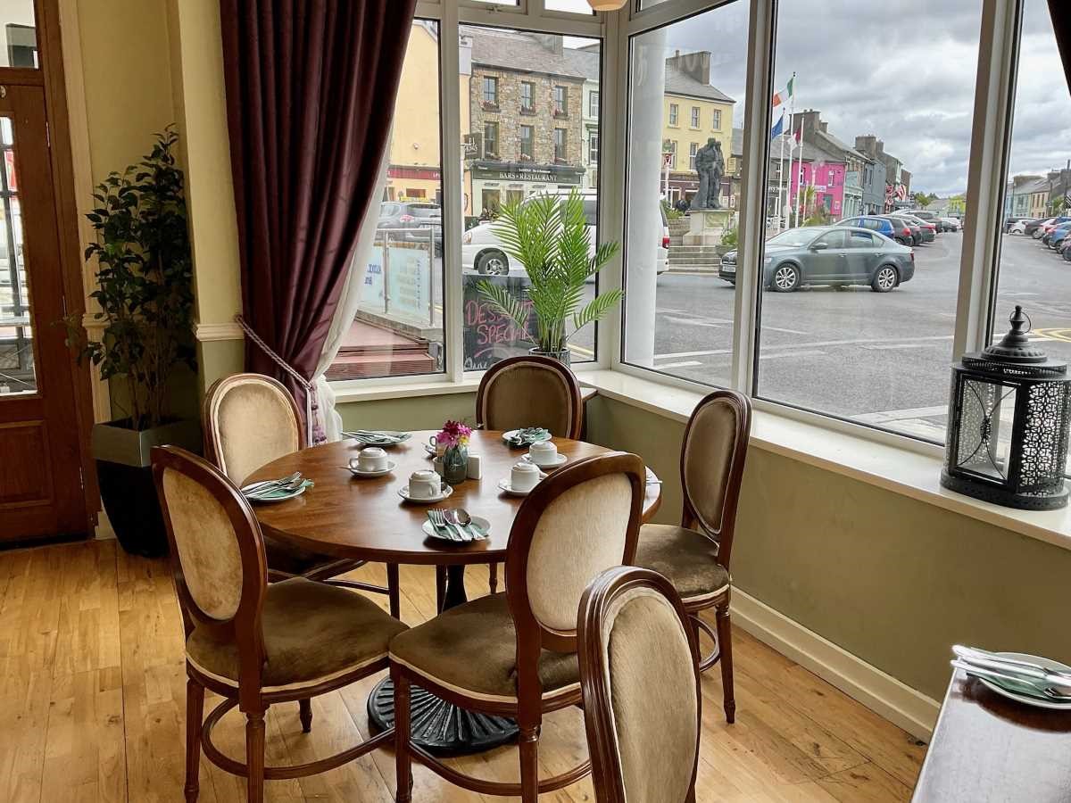 Cozy cafe interior with a round table, chairs, and large windows overlooking a street.