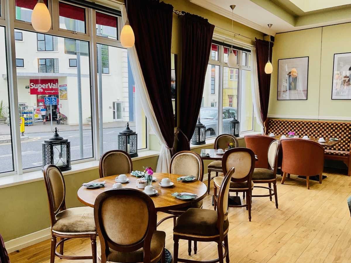 Cozy cafe interior with wooden tables, chairs, and large windows overlooking a street.