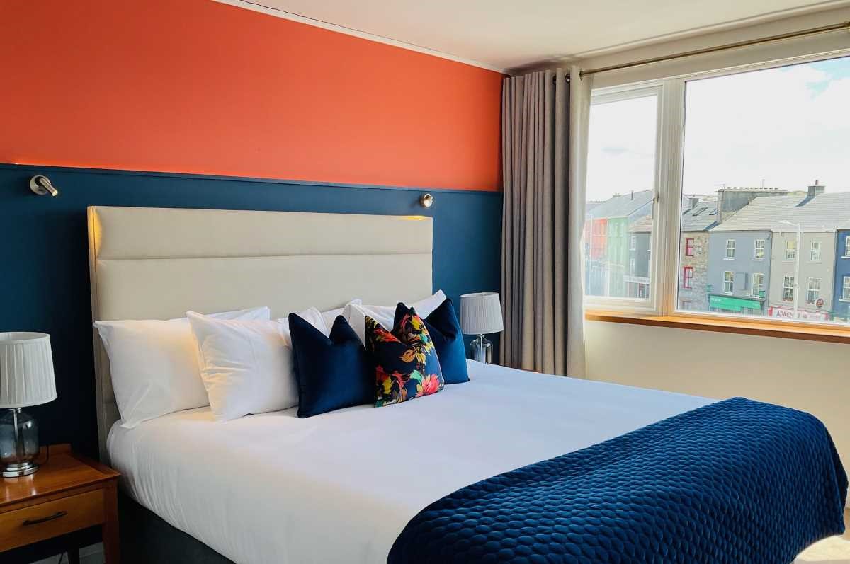 Modern hotel room with colorful pillows, large window, and city view.
