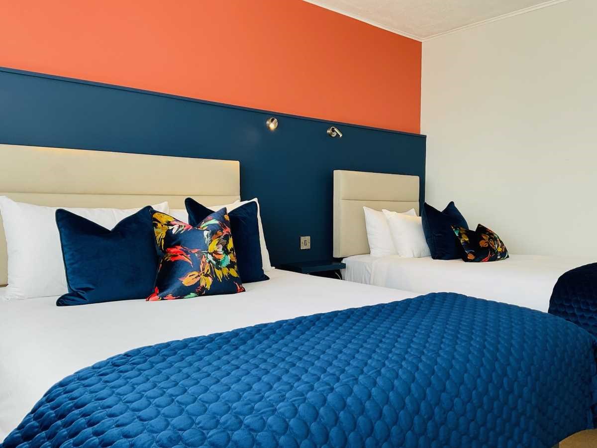 Two beds with blue and floral pillows against a blue and orange wall.