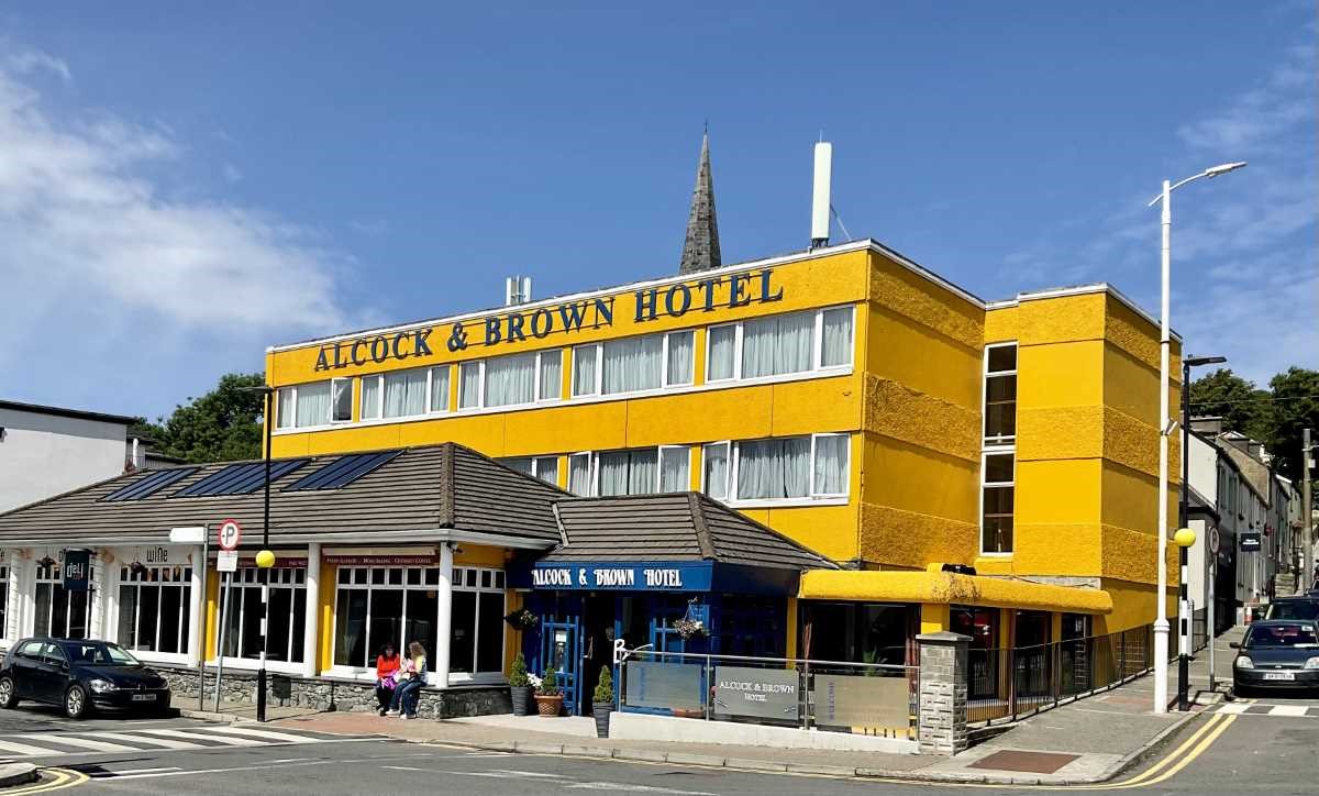 Yellow hotel building with 'Alcock & Brown Hotel' sign, located on a street corner.